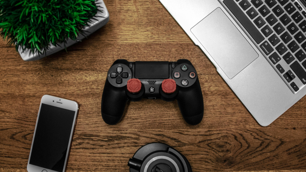 Electronics What to sell on Shopify A gamepad, laptop, headphones, green plant, and mobile phone on a wooden surface.