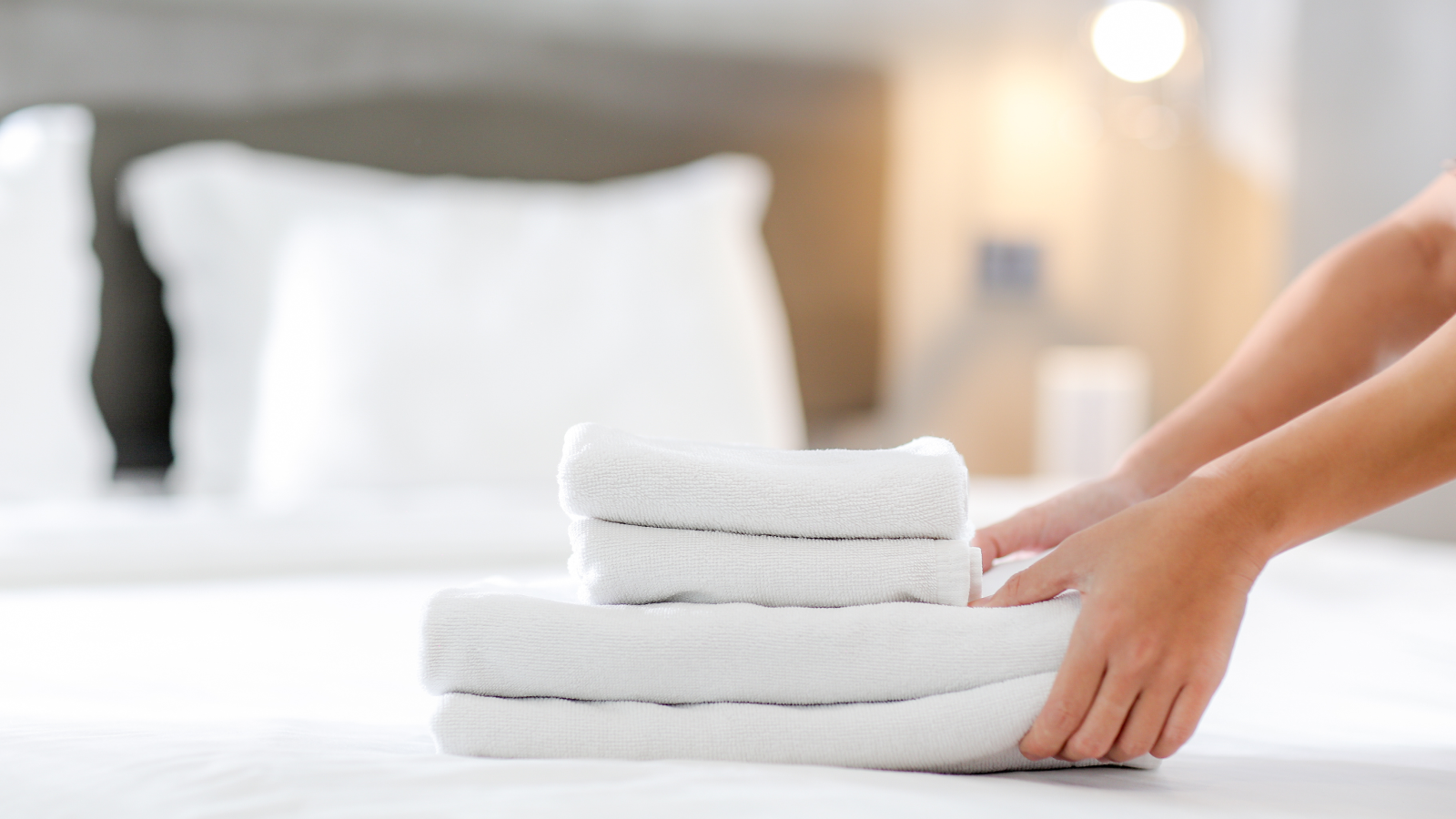 Home and kitchen What to sell on Amazon A person putting together a stack of towels on a bed.