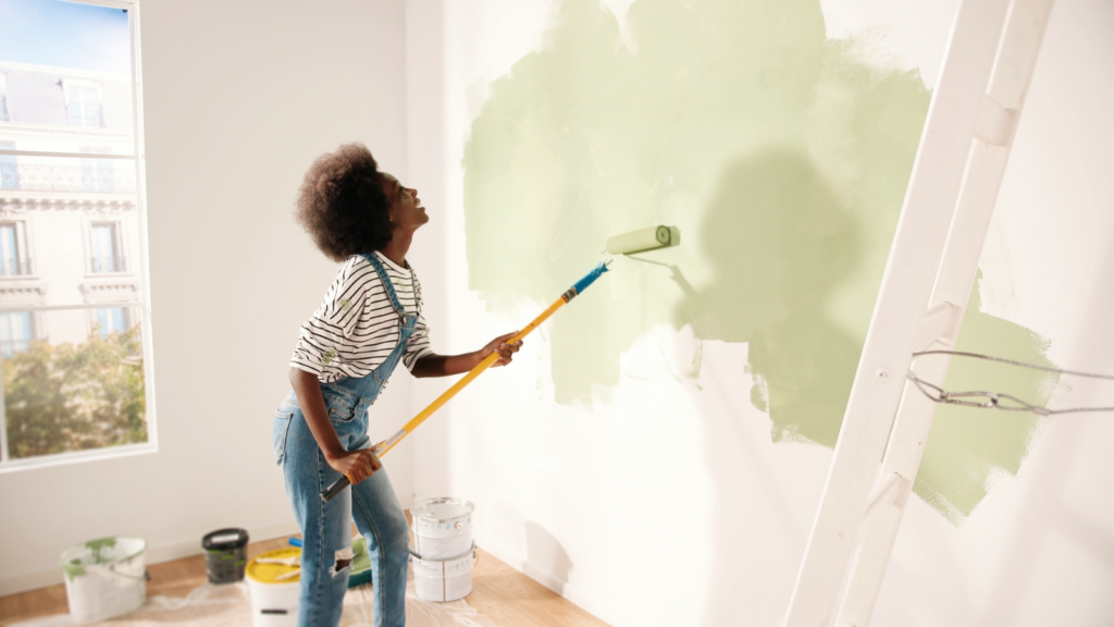 Home improvement services Most profitable businesses A woman painting a green wall with a paintbrush, focused on her task in a well-lit room.