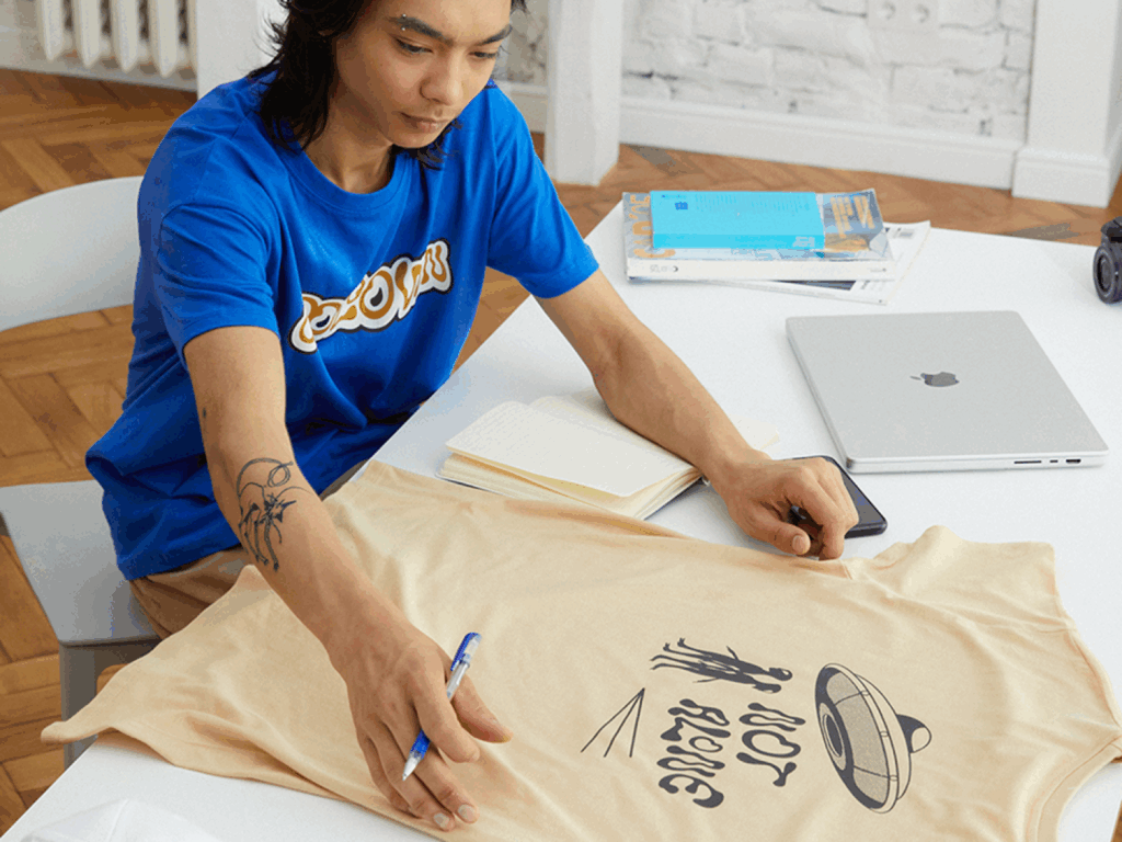 How to create t shirts with Printify A young man in a blue t-shirt looking at a custom beige t-shirt.