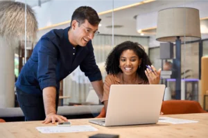 A man and woman smile at a laptop, sharing a moment of joy and engagement together.