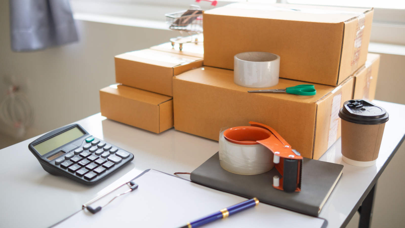 Office products What to sell on Amazon A stack of delivery boxes on top of a table with miscellaneous office supplies around it.
