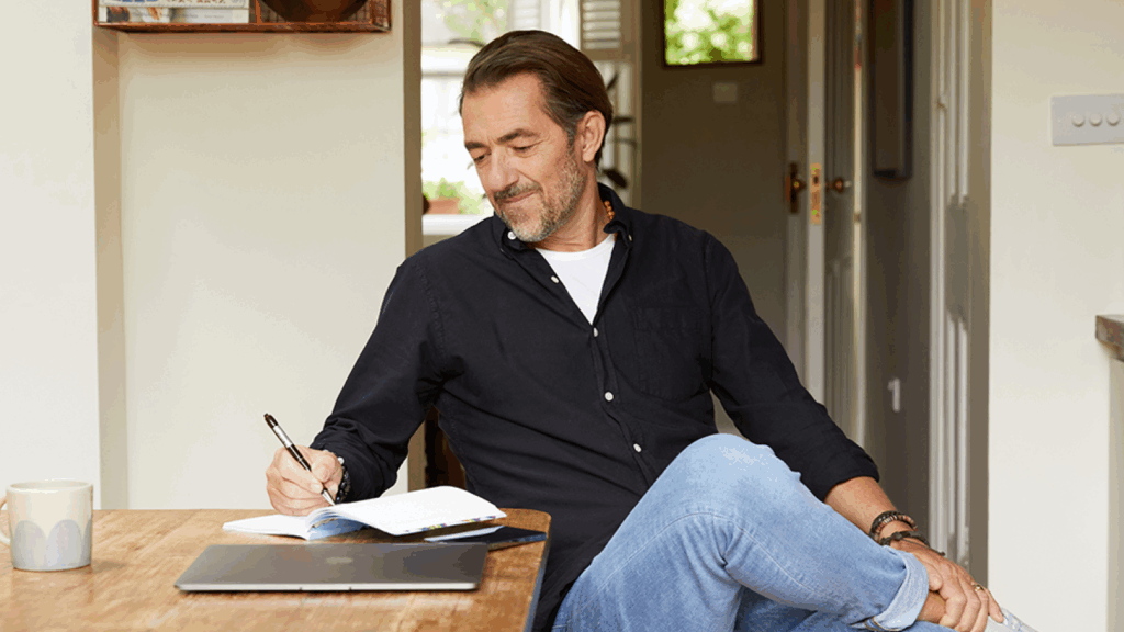 Prepare a TikTok marketing strategy A man in a dark blue t-shirt sitting at a kitchen table, making notes.