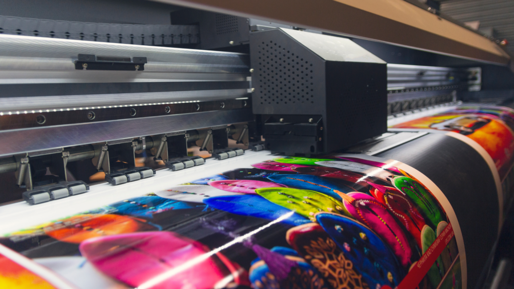 Print on Demand Side hustles that pay well A large print machine actively printing a large sheet of paper with text and images.