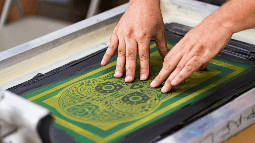 Screen printing Sublimation vs screen printing A person operates a screen printer to create a design in green and yellow colors.