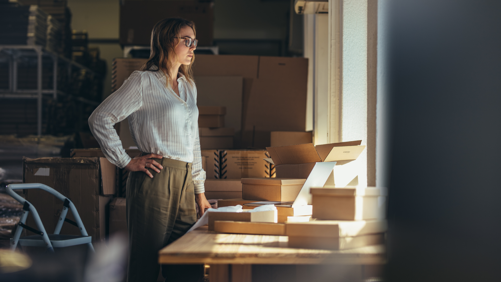 Select a dropshipping supplier How to start a dropshipping business A woman in a white blouse standing in front of a table filled with delivery boxes.