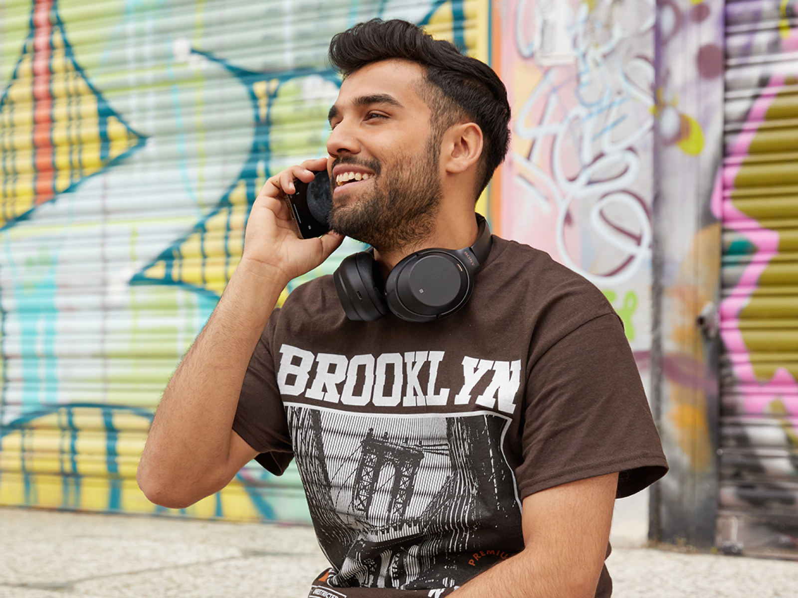 Sell BellaCanvas 3001 t shirts with Printify A man talking on a phone, wearing a brown Bella Canvas 3001 “Brooklyn” t-shirt.