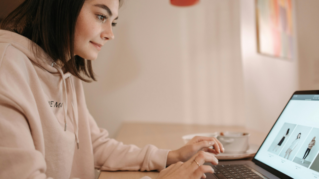 The benefits of selling on a Shopify store A woman in a camel hoodie sitting at a desk and using a laptop.