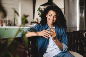 A smiling young woman sitting on a couch, using a mobile phone to set up TikTok for business.
