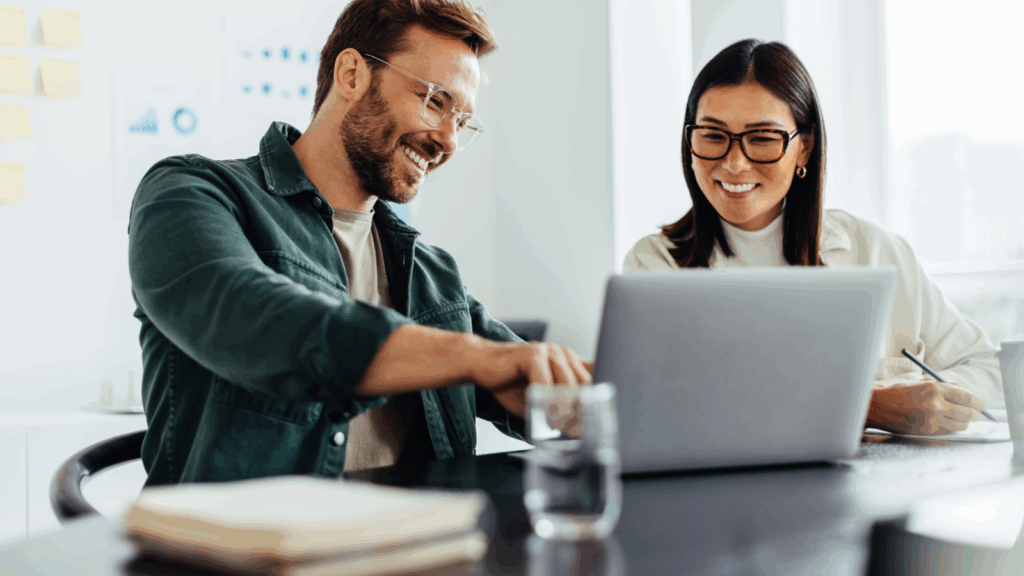 Track financial performance How to start a dropshipping business A smiling man and woman sitting in front of a laptop, with the man pointing at the screen.