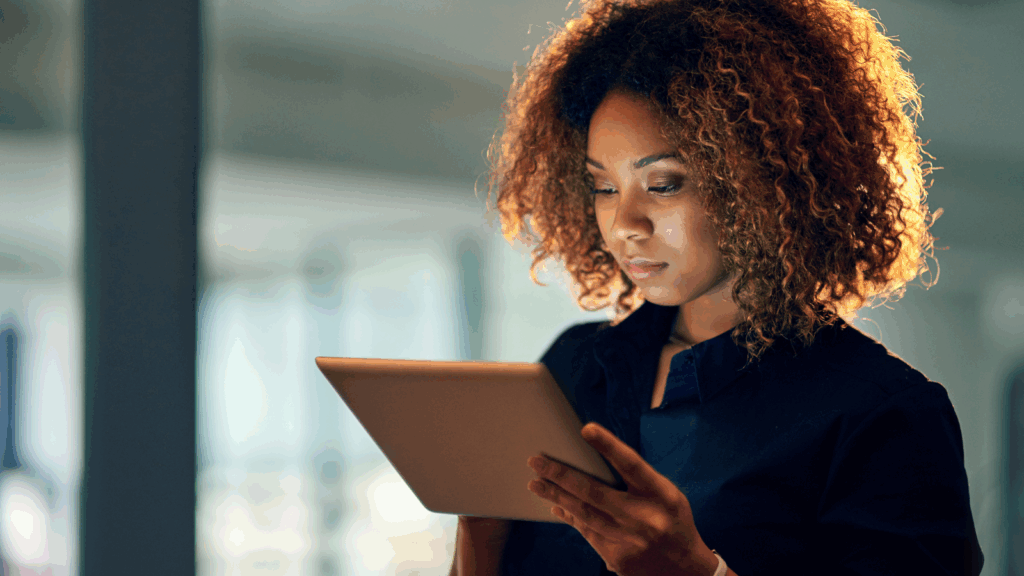 What makes a business successful A woman in a blue blouse standing and looking at a tablet screen.