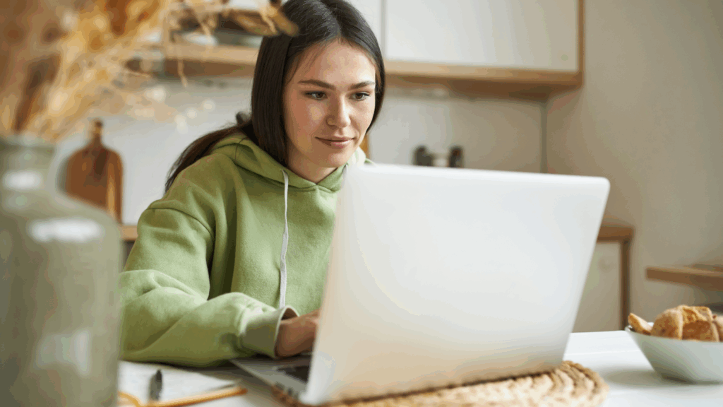 What to consider when selecting products with high profit margins A woman in a green sweatshirt is focused on using a laptop at a desk.