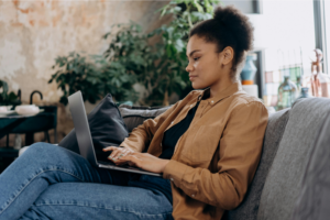 A woman sitting on a couch and using a laptop to find out what to sell on Shopify.