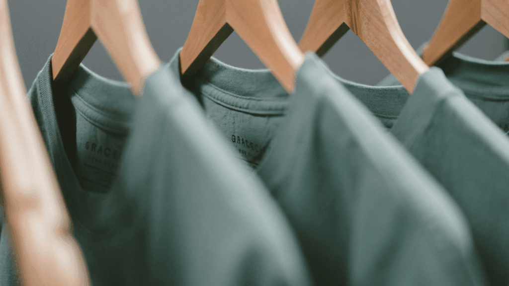 Why t shirt weight matters Green t-shirts displayed on hangers in a retail store, showcasing various styles and sizes.