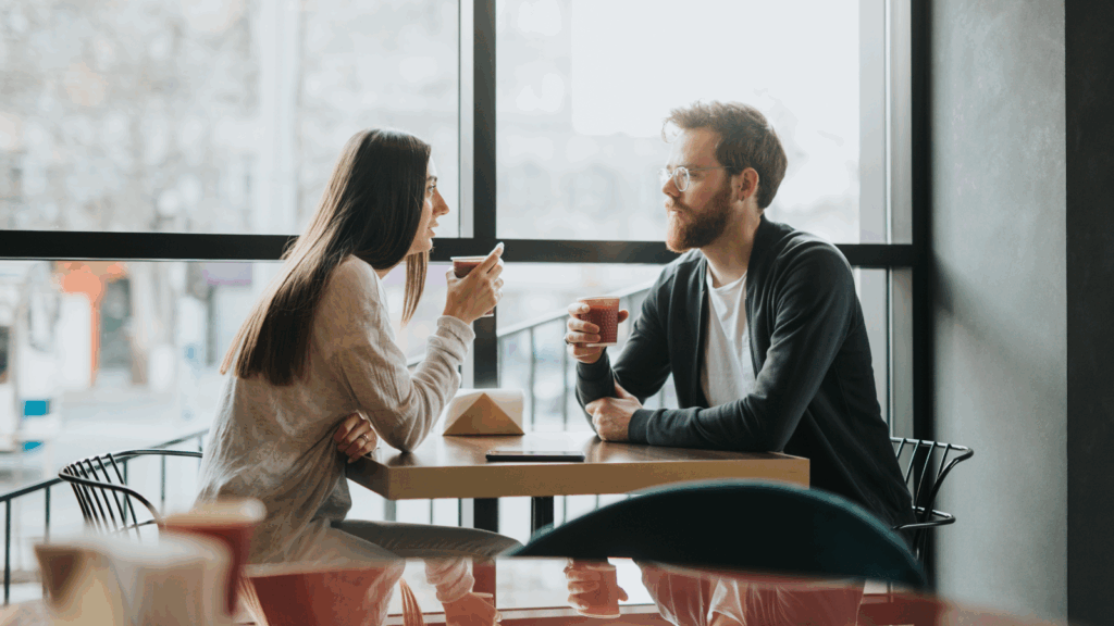 Ask your friends and strangers for input A man and woman seated at a cafe table, engaged in conversation over coffee.