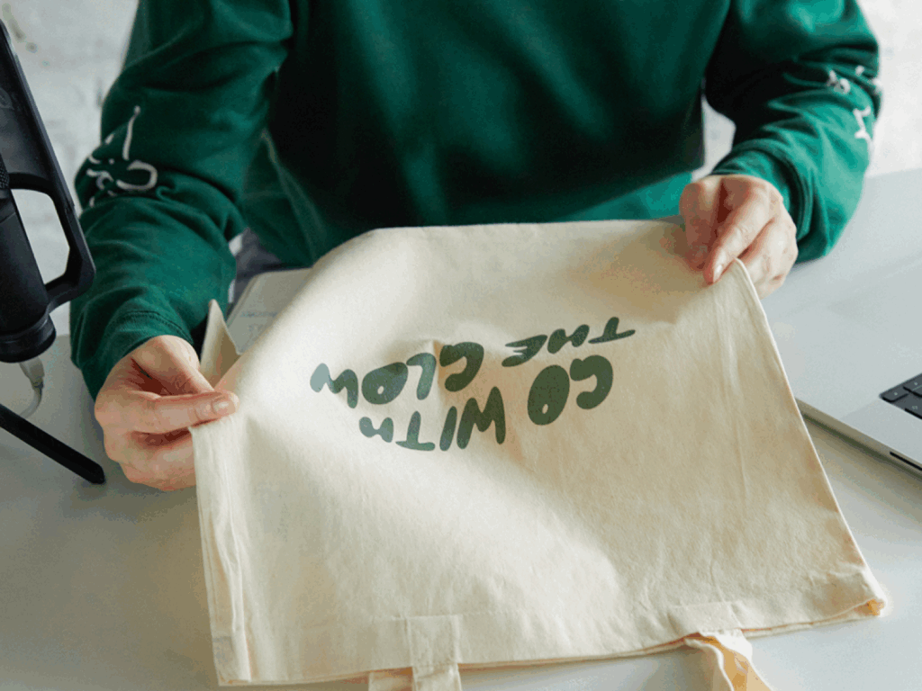 Can you actually make a living with a POD store A woman in a green hoodie holding a custom “Go with the glow” tote bag.