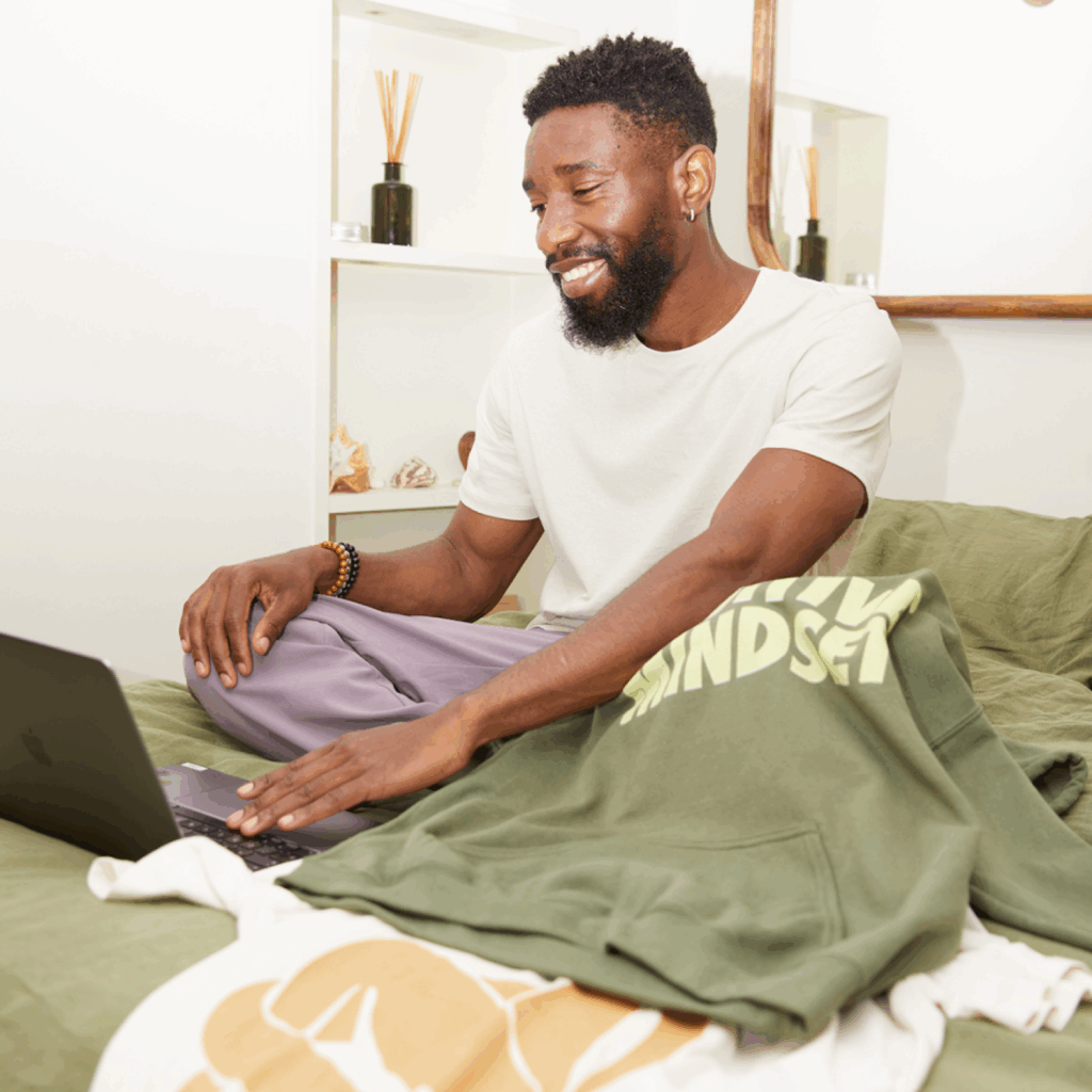 Create and sell custom products with Print on Demand A smiling young man is using a laptop to do print-on-demand as a side business idea.