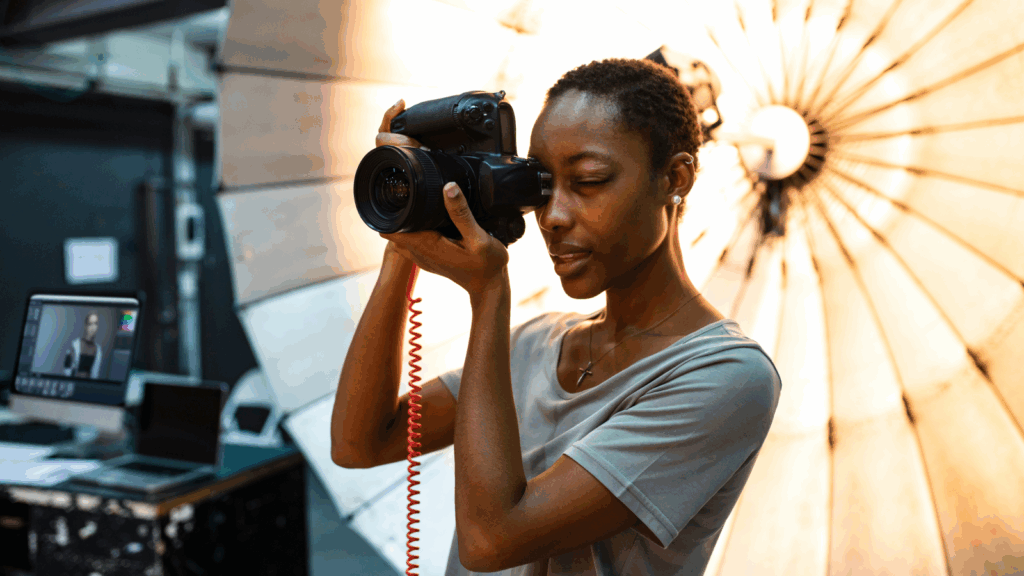 Freelance photography – Shoot portraits products or events A woman holds a camera in front of a bright light, preparing to take a photograph.