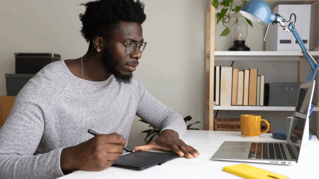 Graphic design services – Design logos websites or templates A man wearing glasses is seated at a desk, working on a laptop.