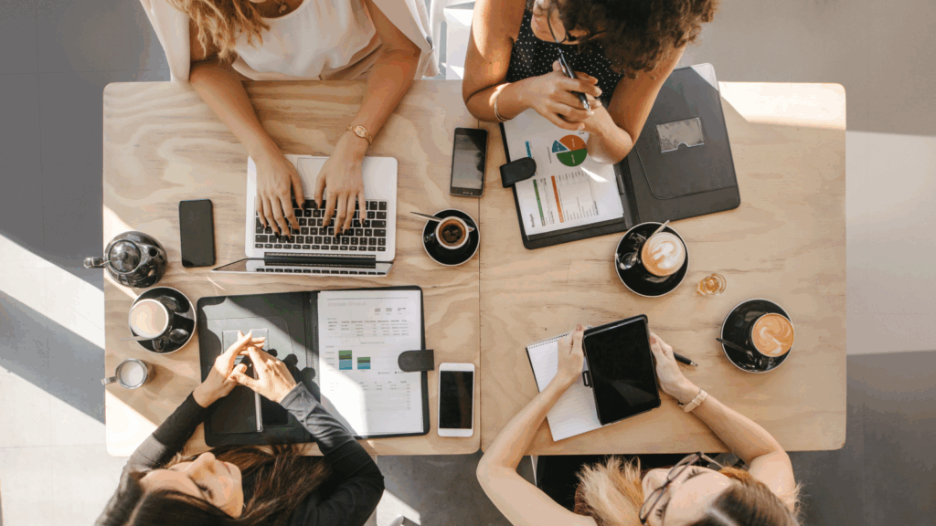 Four women engaged in discussion at a table, each using a laptop for work or collaboration.