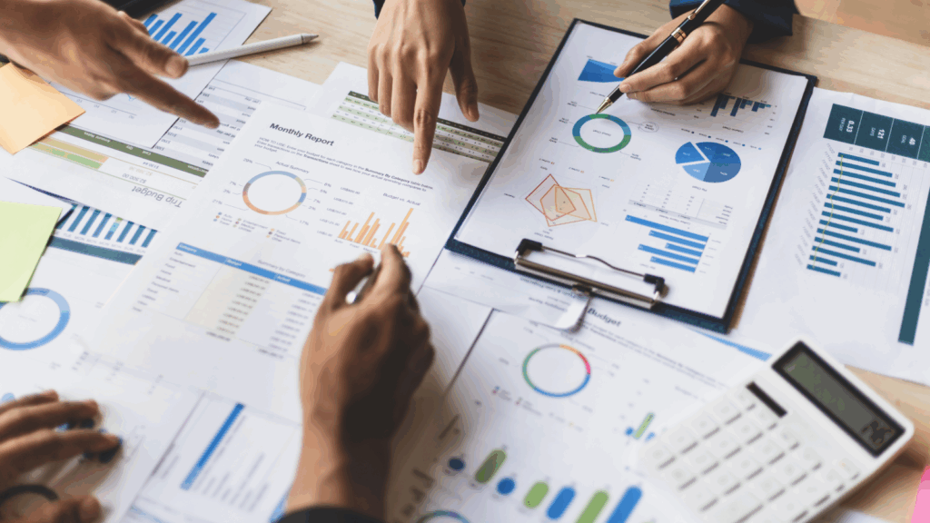 Observe market gaps and customer frustrations Business professionals collaborating at a table, surrounded by papers and calculators, focused on their work.