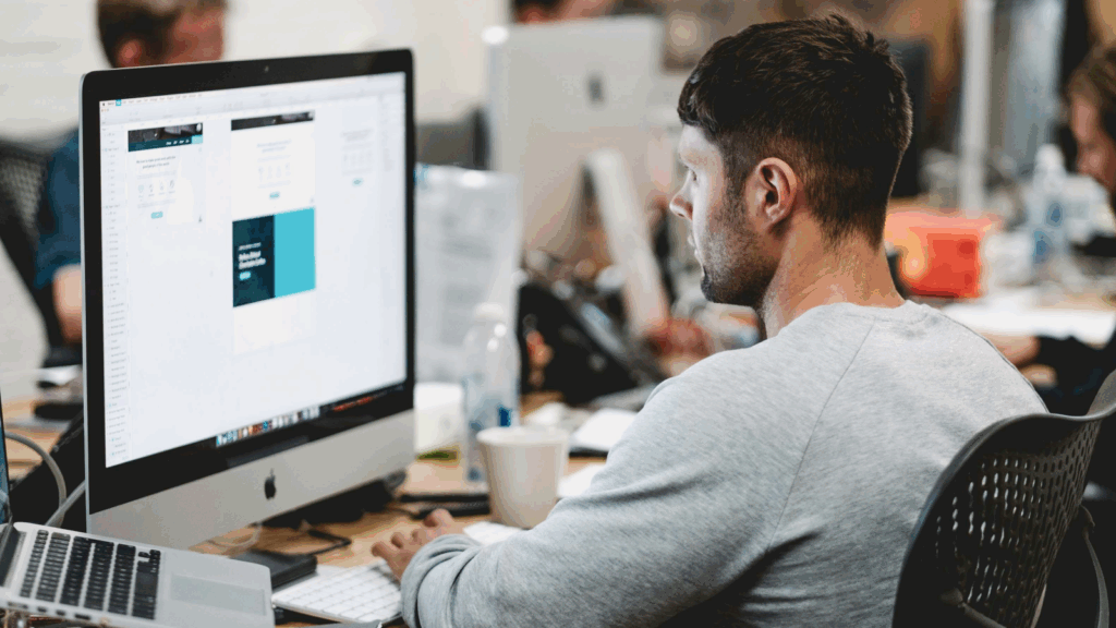 A man is doing graphic design work on a large monitor.