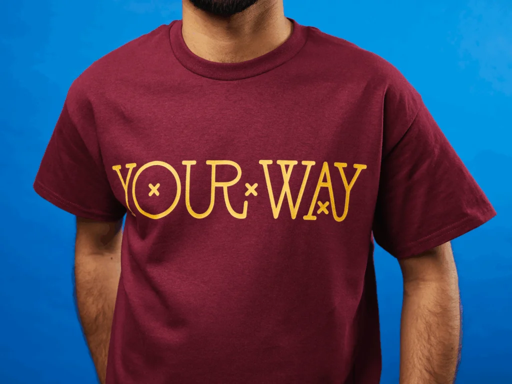 A person wearing a burgundy Next Level 3600 t-shirt with a “Your way” print.