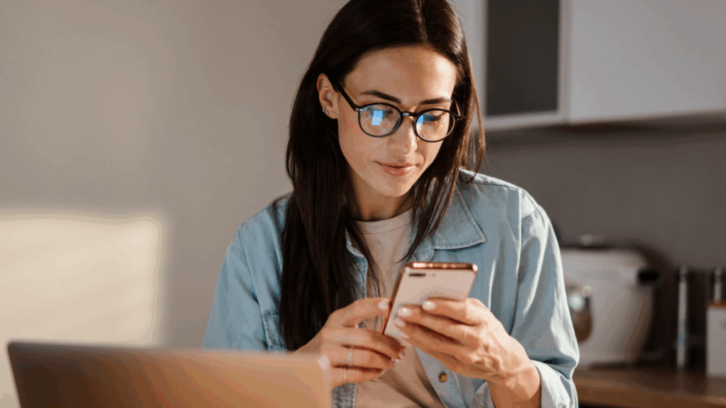 Promote and profit through affiliate marketing A young woman in glasses is using a mobile phone while sitting in front of a laptop.