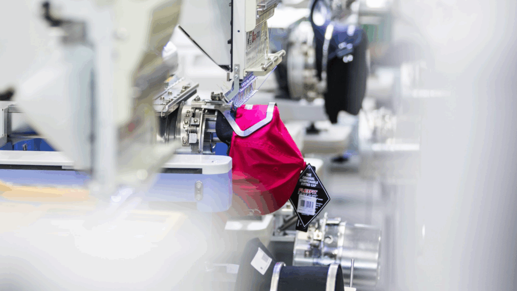 Start a POD business and sell on TikTok with Printify A red bag is hanging on a machine in a factory setting.