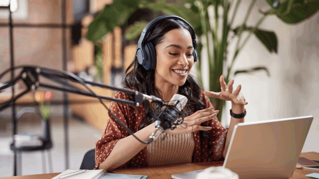 Start a podcast A woman wearing headphones sits at a table with a laptop and microphone, focused on her work.