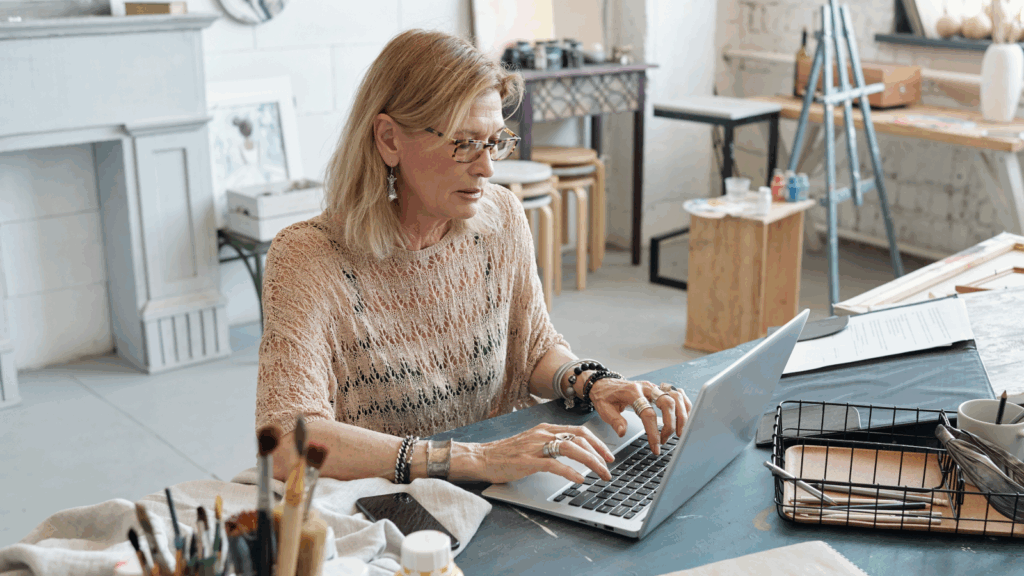 Start selling your art online An older woman is using a laptop in an art studio.