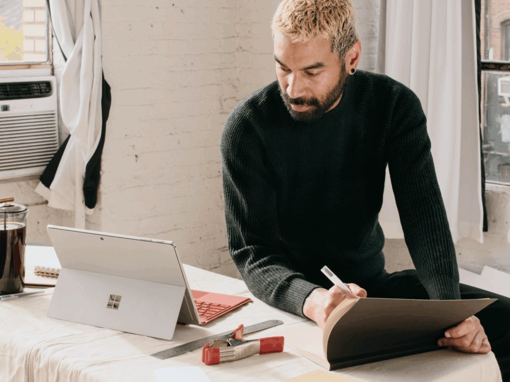 Tips for starting your art business online A young bearded man is making notes from a laptop on “How to make prints of your art”.