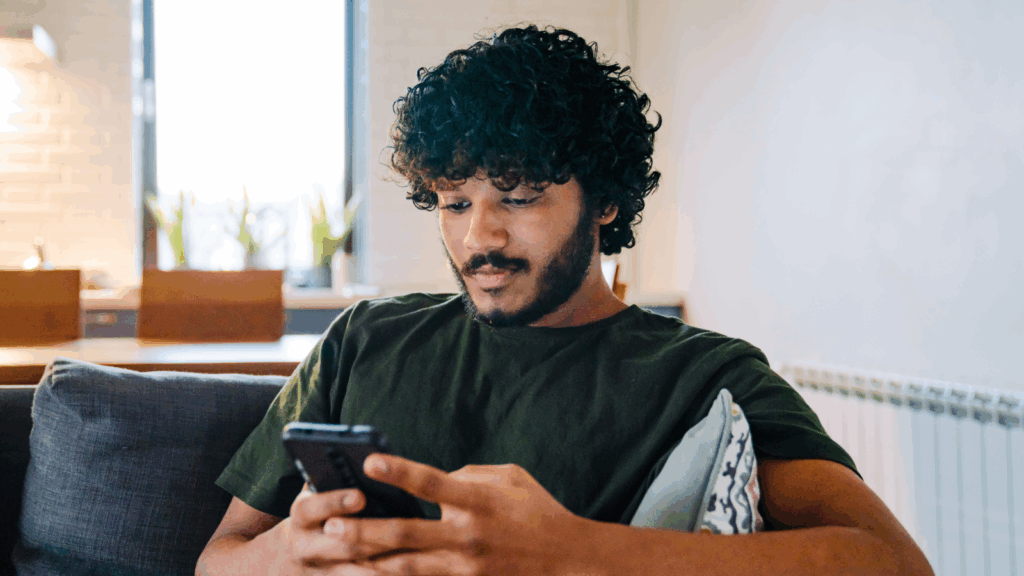 Use social media A young man is sitting on a couch and using a mobile phone to learn how to start dropshipping for free.