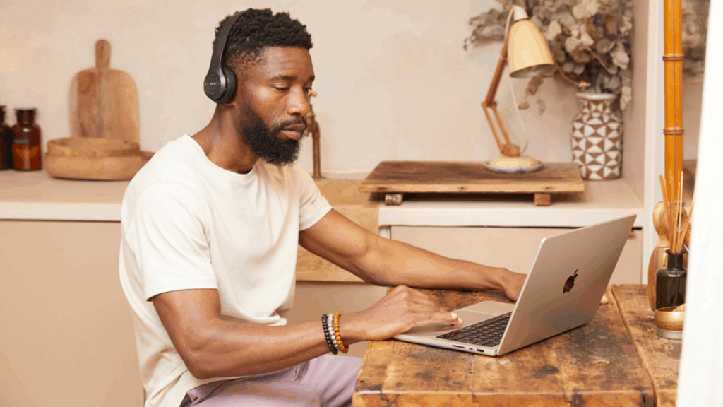 Using Print on Demand A man is sitting at a kitchen table, using a laptop.