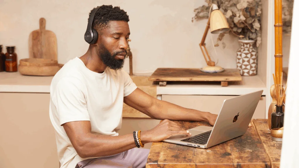 A man is sitting at a kitchen table and using a laptop.