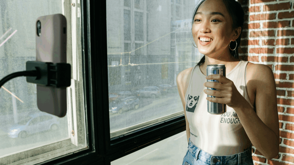A woman holding a canned beverage and recording herself on a mobile phone.