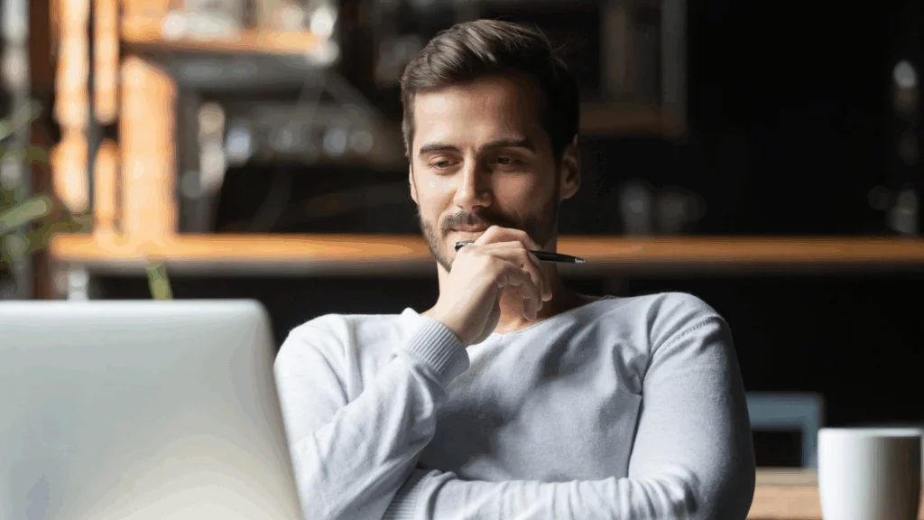 A man is looking at a laptop screen and thinking.