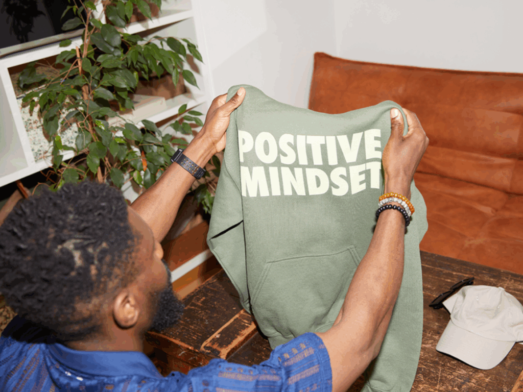 A man is holding a custom green “Positive mindset” hoodie in front of him.