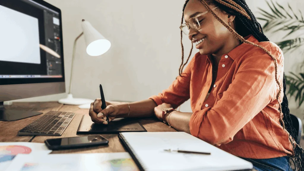 A smiling woman is using a pad to create graphic design elements.