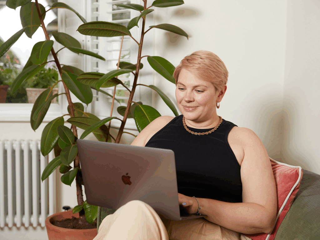 A young woman is sitting in a chair and using a laptop to create and sell merch for nonprofits.