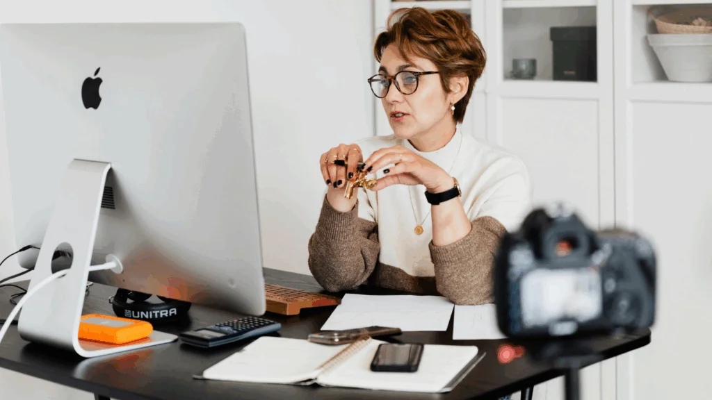 A woman is sitting in front of a monitor and recording herself to sell online courses.