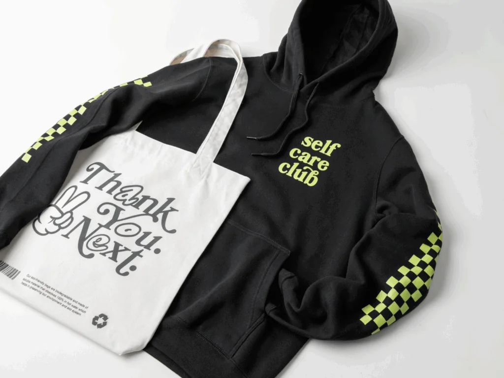 A black “Selfcare club” hoodie and a “Thank you. Next” tote bag on a white background.