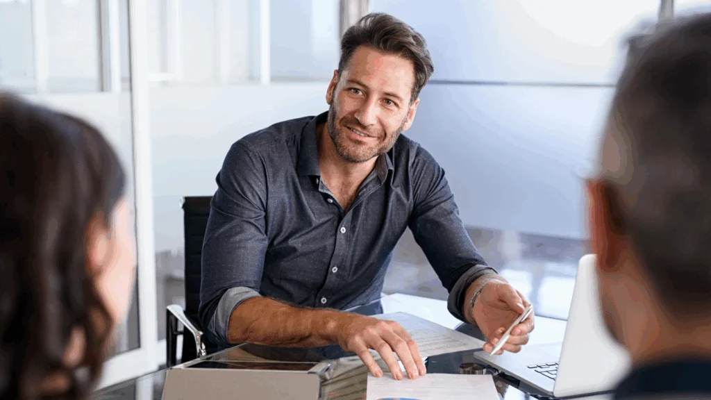 A man sits at a table with two other people, engaged in conversation.