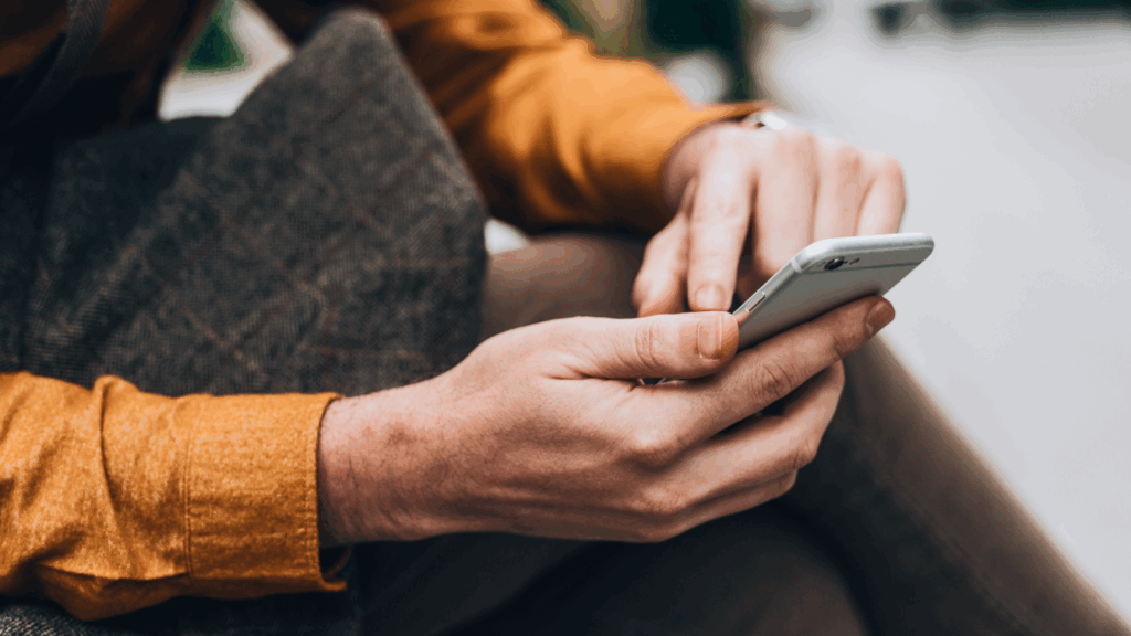 A person sitting on a bench, holding a cell phone and looking at the screen.