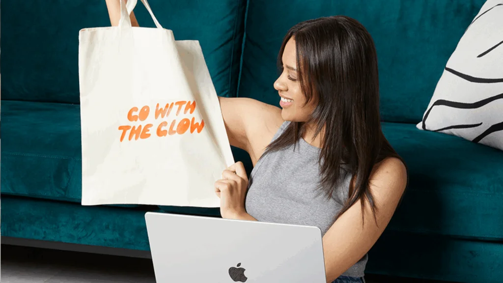 A woman sitting on a couch, smiling while holding a shopping bag in her lap.