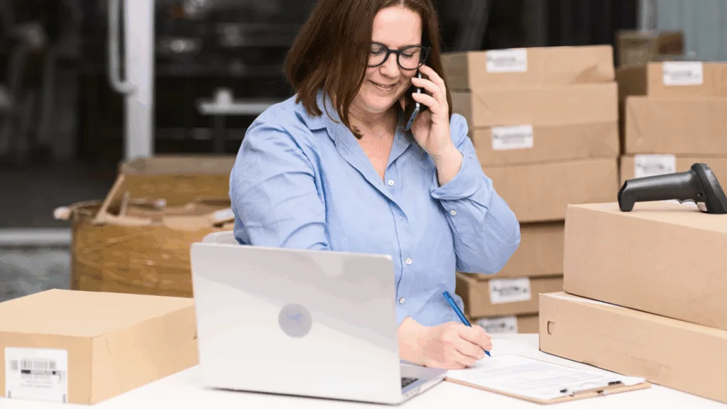 A woman wearing glasses sits at a desk with a laptop and several boxes organized around her.