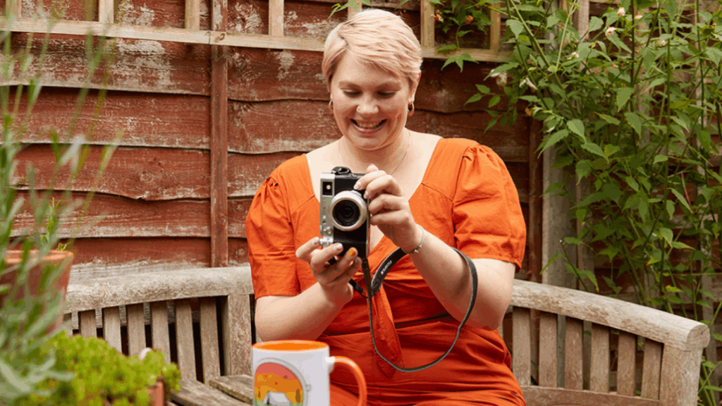 A woman in an orange dress holds a camera, ready to capture a moment.