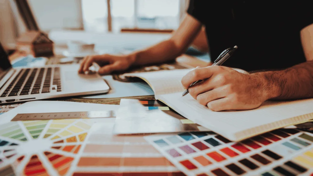 A person working on a project at a laptop, surrounded by various color swatches for design inspiration.
