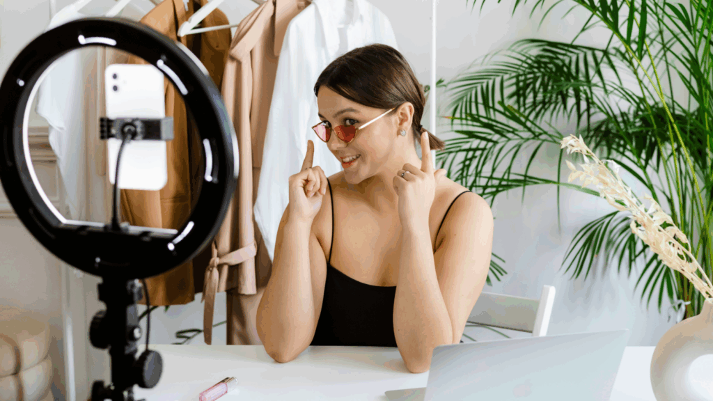 A woman sitting at a desk, working on a laptop with a camera positioned nearby.