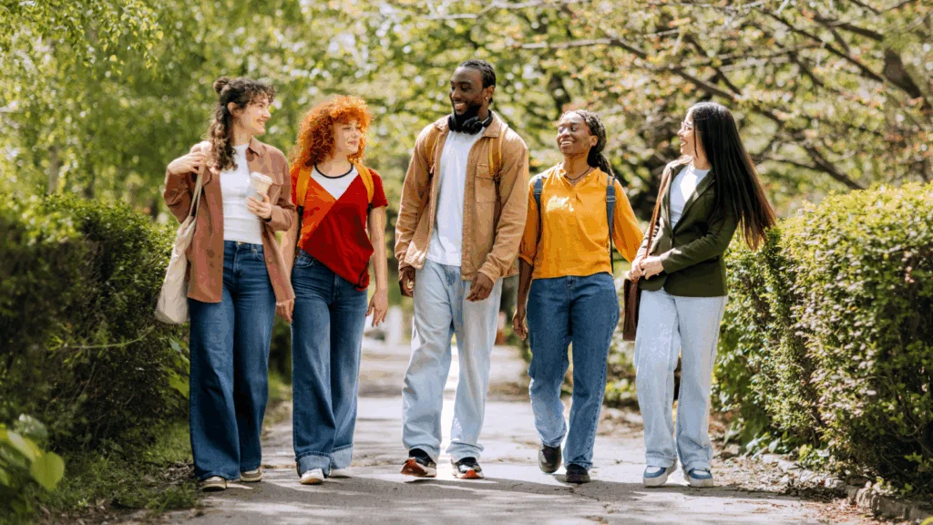 A group of young people walking together, enjoying a sunny day in the park, surrounded by greenery and trees.